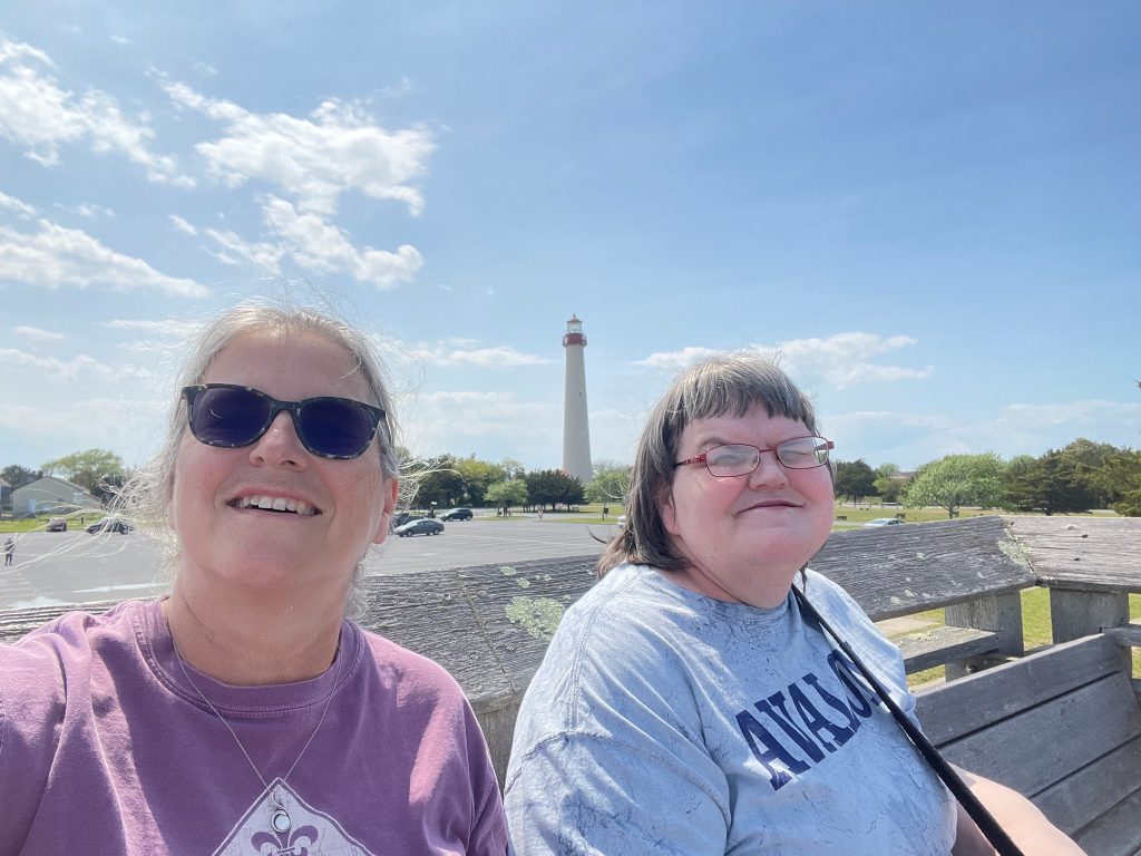 A female advocate and her female partner sit on a bench in front of the Cape May, New Jersey lighthouse